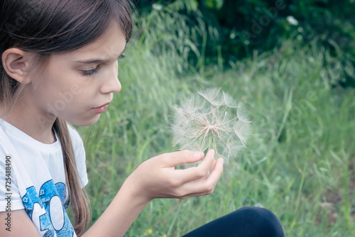 Closeup portrait of a beautiful little girl on the background of a green field with a big dandelion in her hand
