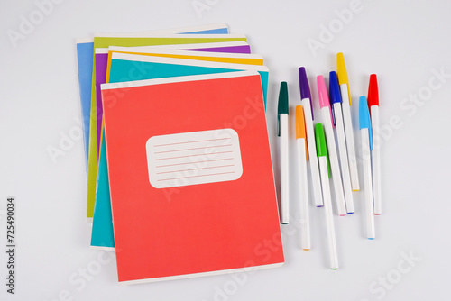 A stack of colorful school notebooks lies chaotically with pens, highlighted on a white background.Purchase, sale of school supplies, stationery store.The template for the logo. Copyspace