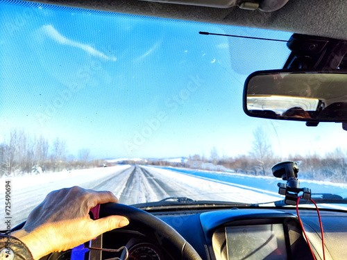 Hand of woman on the steering wheel in a car and view through the windshield of a winter road with snow-covered trees