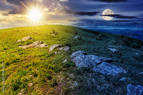mountain landscape with stones among the grass on top of the hillside beneath a sky with sun and moon at twilight. day and night time change concept. mysterious countryside scenery in morning light