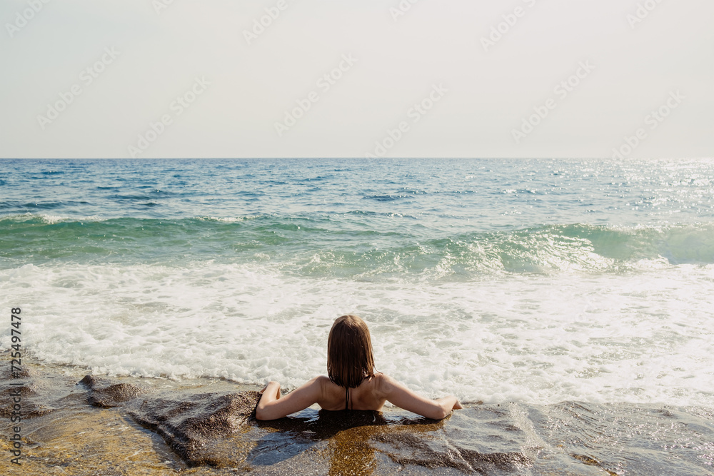 A contemplative woman sits by the seashore, the ocean's expanse before her, in a moment of serene solace