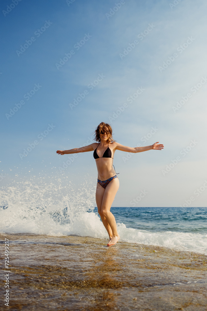 A joyful woman dances in the sea, splashes surrounding her, under a bright blue sky A joyful woman dances in the sea, splashes surrounding her, under a bright blue sky