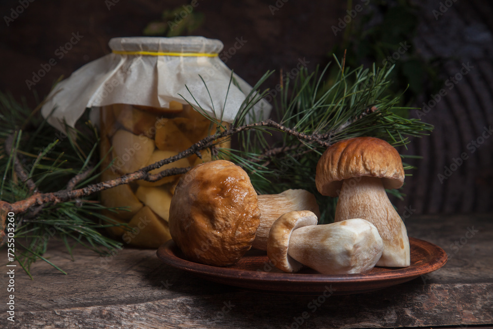 Clay plate with three porcini mushrooms commonly known as Boletus Edulis and glass jar with canned mushrooms on vintage wooden background.. Clay plate with three porcini mushrooms commonly known as Boletus Edulis and glass jar with canned mushrooms on vintage wooden background..