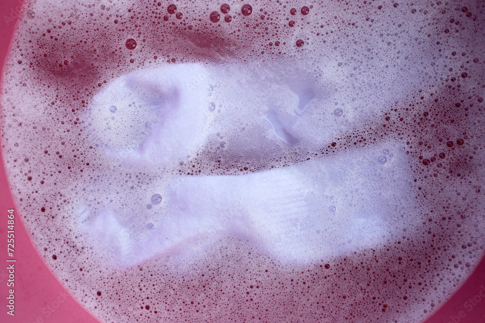 Fototapeta premium Dirty socks soaked in water, dissolving detergent in basin.