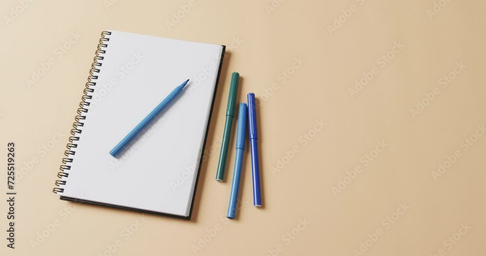 Close up of blue markers with notebook with copy space on beige background, in slow motion Close up of blue markers with notebook with copy space on beige background, in slow motion