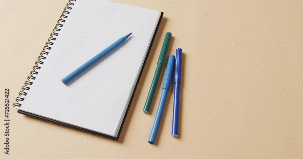 Close up of blue markers with notebook with copy space on beige background, in slow motion Close up of blue markers with notebook with copy space on beige background, in slow motion
