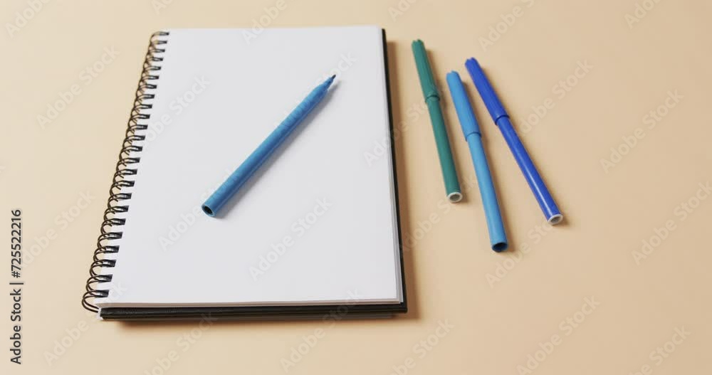 Close up of blue markers with notebook on beige background, in slow motion Close up of blue markers with notebook on beige background, in slow motion