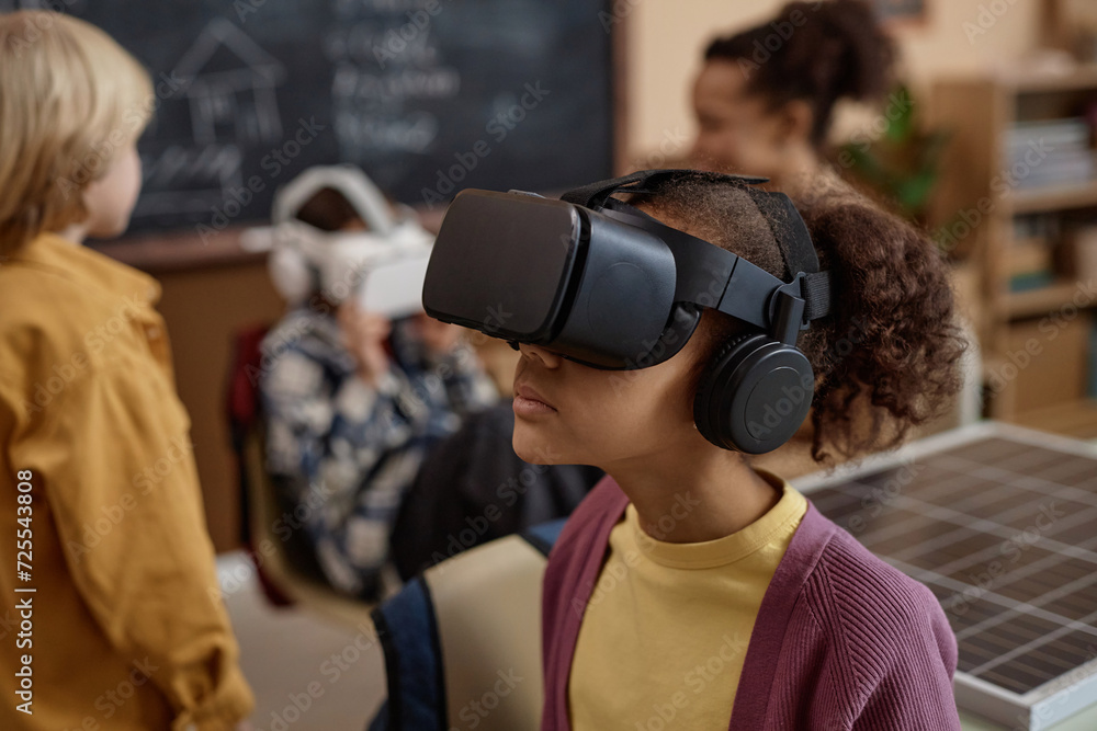 Side view portrait of young Black girl wearing VR headset in class and enjoying immersive learning experience copy space