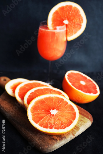 Grapefruit juice in a glass next to sliced ​​grapefruit on a dark background