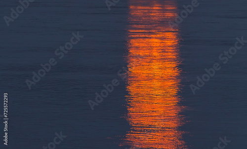 Abstract dark blue water background with red and golden colored reflections on surface.