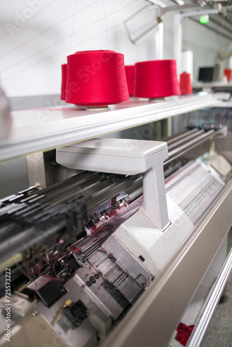 Obraz na plátně Automated flat knitting machine manufacturing textile with red yarn spools in a factory