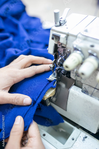 Closeup of tailor hands sewing blue fabric with an industrial overlock machine.