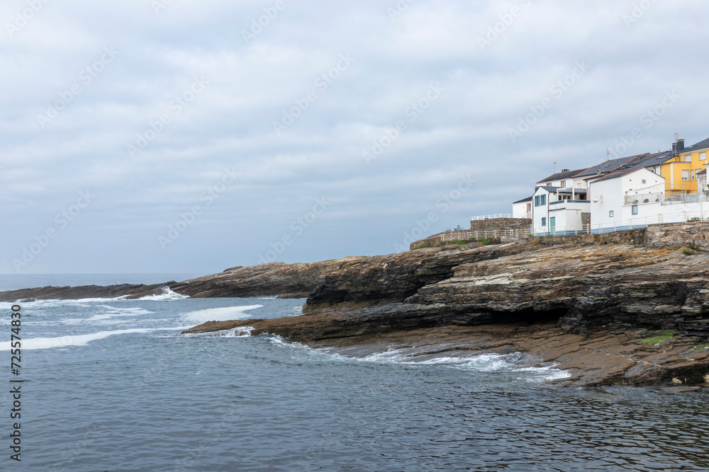 A serene coastal landscape with houses perched atop rugged shores, gentle ocean waves, and an overcast sky