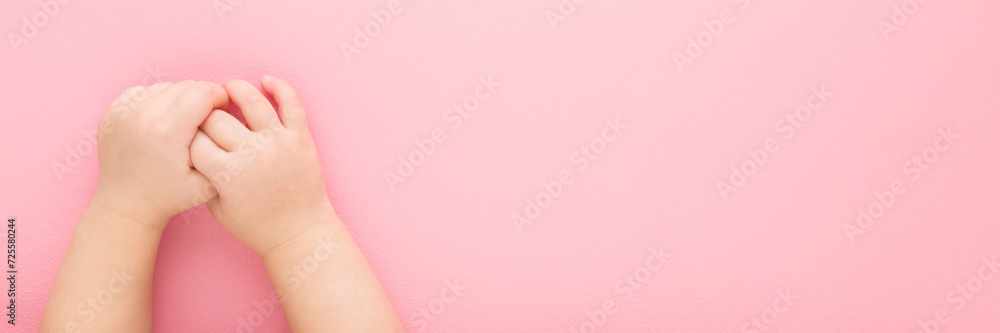 Baby girl hands on light pink table background. Pastel color. Closeup. Point of view shot. Empty place for text. Wide banner. Top down view. - obrazy, fototapety, plakaty 
