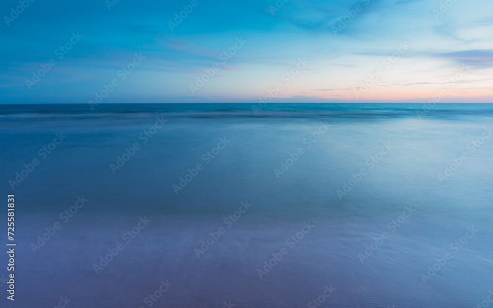 The sea is calm. The sand and water surfaces are smooth. There are no people. blurred motion