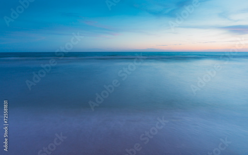 The sea is calm. The sand and water surfaces are smooth. There are no people. blurred motion