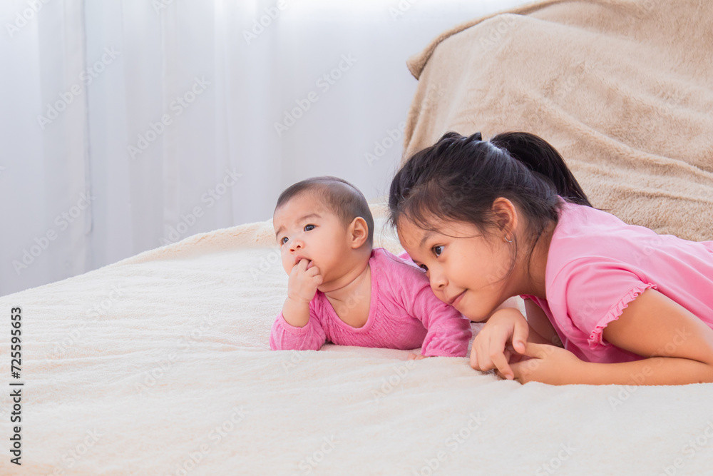 Asian sibling love bonding relationship, adorable girl playing with toddler younger sister on bed soft touching, happy kids nursing hugging embracing together, preschool girl spend holiday at home