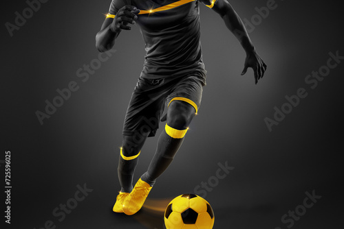 Cropped image of male soccer playing in motion, dribbling ball over dark background. Yellow elements. Monochrome. Concept of competition, tournament, match, game. Creative design.