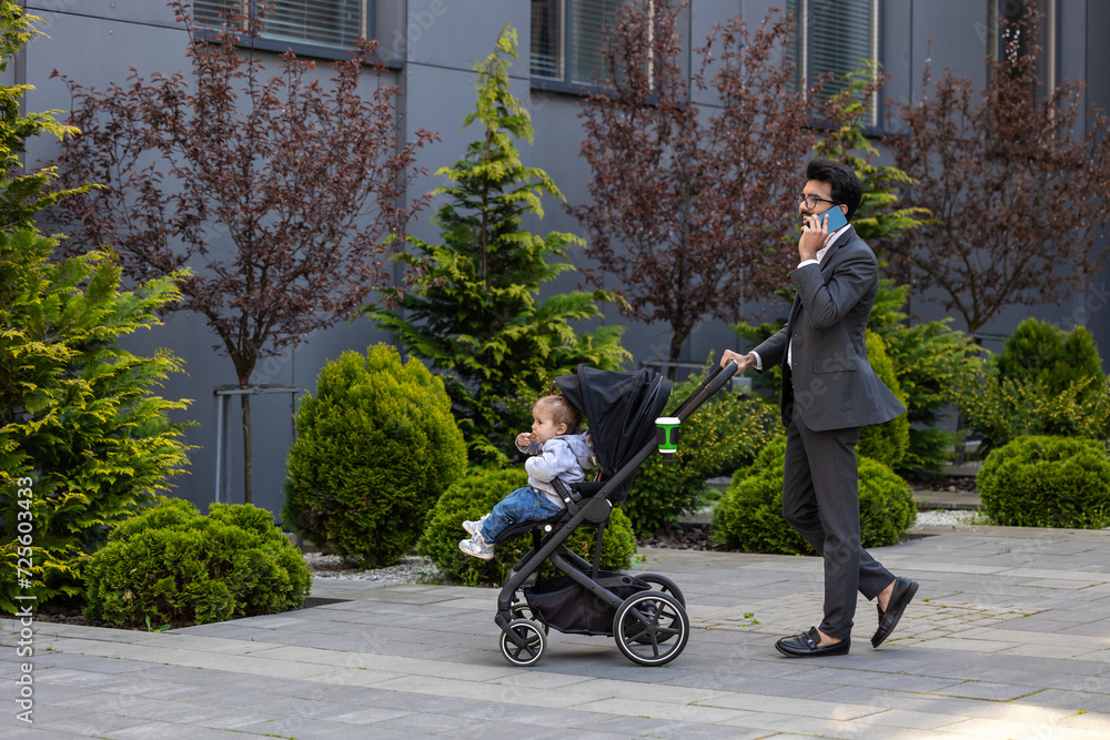 Elegant young man talking on the phone and carrying a baby carriage