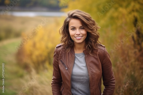 Fashionable woman in a brown leather bomber jacket taking a leisurely stroll on a rural path surrounded by autumn leaves