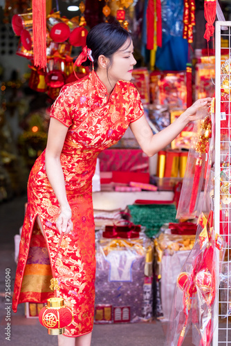 Asian woman in red cheongsam dress choosing and buying home decoration and ornament for celebrating Chinese Lunar New Year festival at market.Celebrate Chinese lunar new year.Celebrate season holiday.