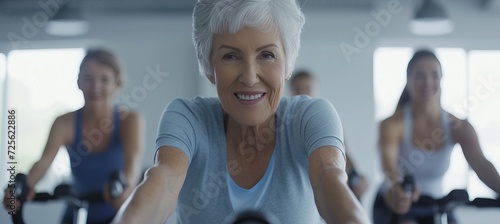 Energetic senior woman with gray hair cycling with group on indoor exercise bike in gym