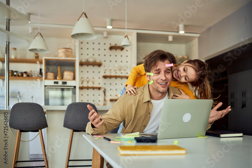Stay-at-home dad trying to work on his laptop while being distracted by his small daughter. photo