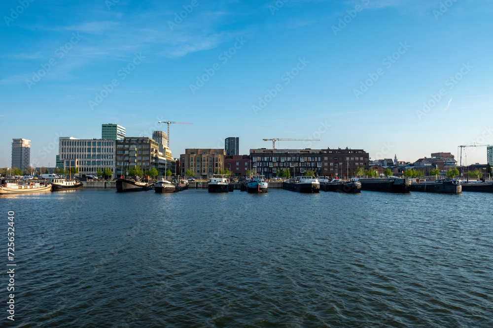 Antwerp, 20th of April, 2022, This image offers a daytime view of Antwerp's modern waterfront. The composition is centered on the calm waters of the port with various boats moored along the dock. The