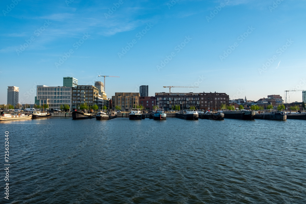 Antwerp, 20th of April, 2022, This image offers a daytime view of Antwerp's modern waterfront. The composition is centered on the calm waters of the port with various boats moored along the dock. The Antwerp, 20th of April, 2022, This image offers a daytime view of Antwerp's modern waterfront. The composition is centered on the calm waters of the port with various boats moored along the dock. The