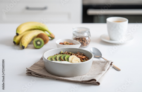 Baked granola with banana and kiwi on the table with cup of tea on a white kitchen background.