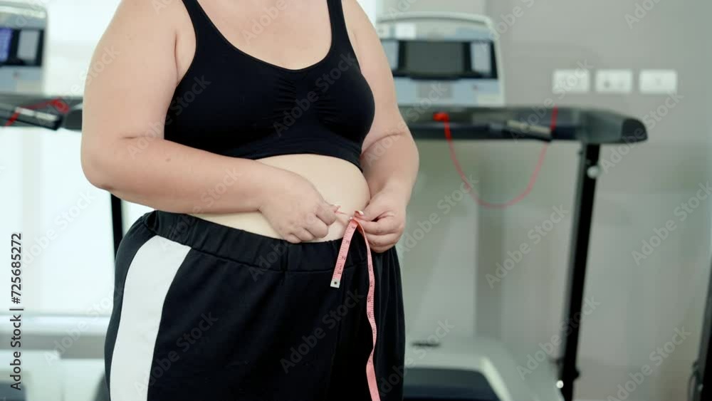 Medium Shot, chubby Asian woman wearing exercise clothes for good exercise, using hand-holding waist measurement tape measure own waist circumference, knowing results before, after exercise. Medium Shot, chubby Asian woman wearing exercise clothes for good exercise, using hand-holding waist measurement tape measure own waist circumference, knowing results before, after exercise.