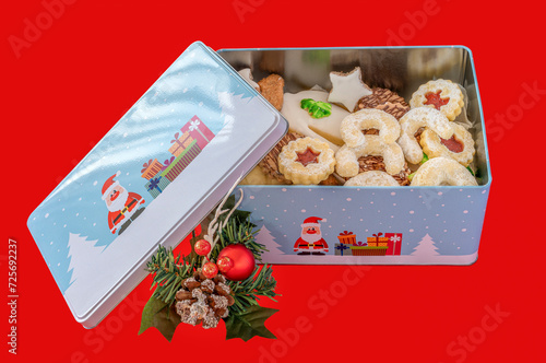 Weihnachtsbäckerei in einer bunten Keksdose mit  Weihnachtsdekoration vor einem roten Hintergrund