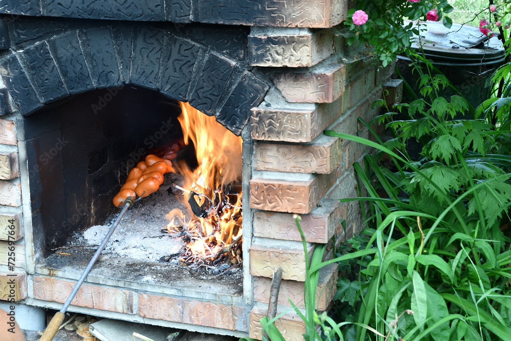 Man roasts meat sausages in a brick fireplace at the cottage