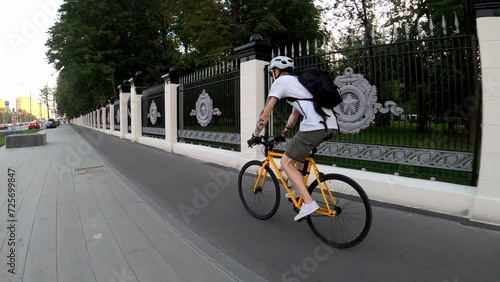 Cyclist rides on asphalt road in the summer among the street. Back view