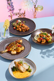 Stylish seafood ensemble featuring a grilled fish with caramelized onions and seared scallops on a creamy sauce, beautifully accompanied by a vibrant floral arrangement