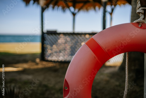 Sotogrante, Spain - January 25, 2024 - A close-up of a red lifebuoy with a blurred beach hut and sea in the background.