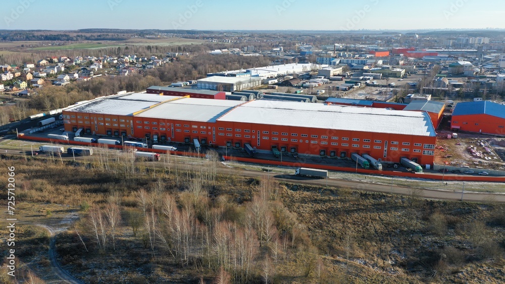 A long, huge logistics center made of orange-colored metal, a large warehouse, a place to store retailers' goods outside the city, near a metropolis. A long, huge logistics center made of orange-colored metal, a large warehouse, a place to store retailers' goods outside the city, near a metropolis.