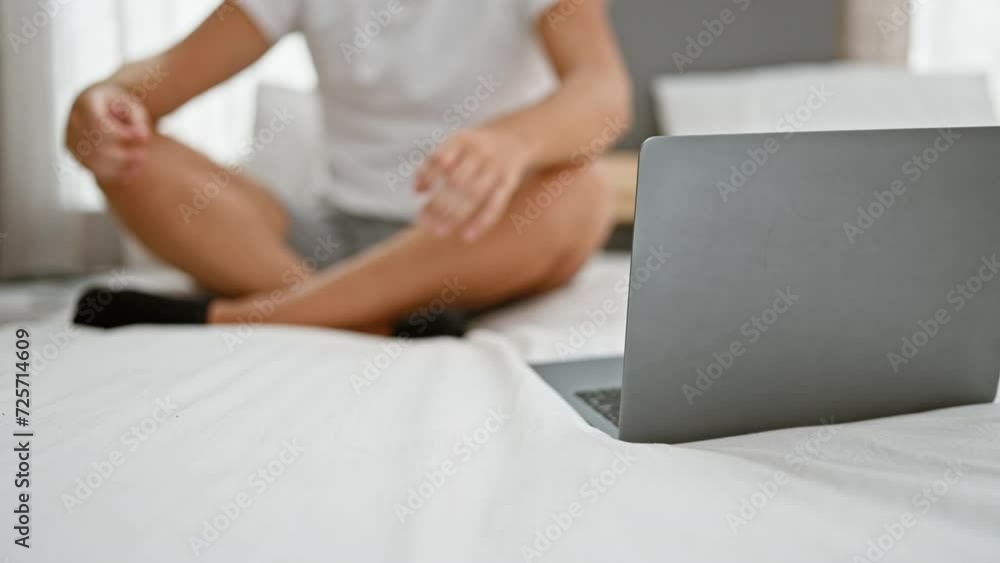 Young adult man meditating on bed in front of laptop inside a bedroom, embodying tranquility and digital lifestyle at home Young adult man meditating on bed in front of laptop inside a bedroom, embodying tranquility and digital lifestyle at home