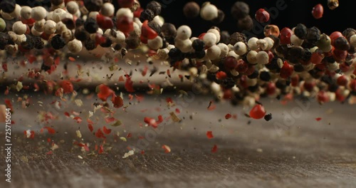 Super slow motion macro of dry mixed flavorful and aromatic peppercorn seeds is flying isolated on soft rustic wood background at 1000fps. photo