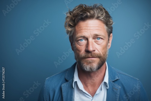 Portrait of a handsome mature man with a beard and mustache in a blue shirt on a blue background. © Juan Hernandez