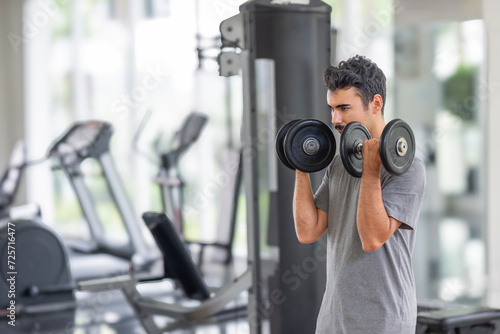 A determined male athlete in focused concentration, performing bicep curls with heavy dumbbells in a sunlit gym. Perfect for themes of dedication and personal fitness. Dedication to Fitness concept..