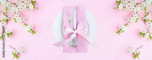 White plate, knife, fork and white flowering tree branches on the pink background. Top view. Copy space.