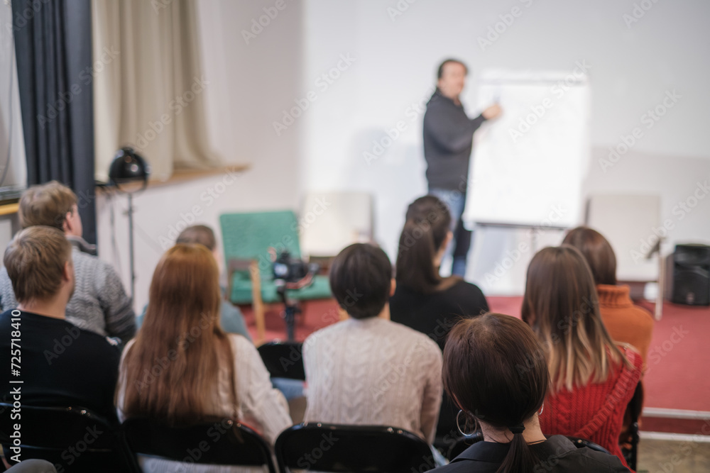 Rear view of participants focused on a presenter at a business workshop, capturing the concept of corporate training.