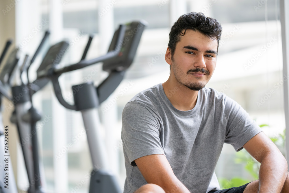 Smiling young man resting after a workout in a gym with exercise machines in the background Smiling young man resting after a workout in a gym with exercise machines in the background