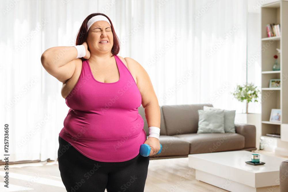 Plus size woman with a dumbbell holding her stiff neck Plus size woman with a dumbbell holding her stiff neck