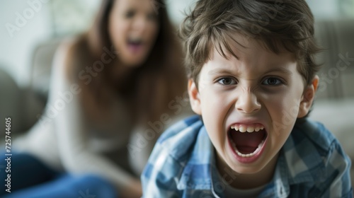 A little boy screams in hysterics, displaying childish aggression against the background of his mother photo