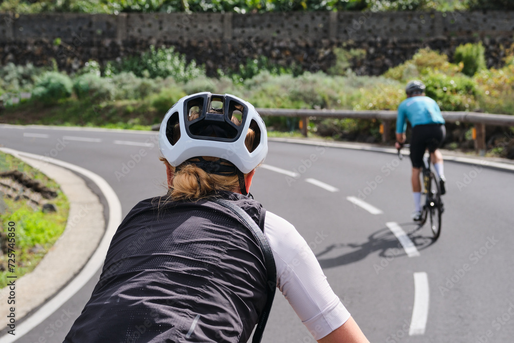 Close-up rear view of a woman and a man cycling on an empty mountain road on Tenerife. Cycling adventure. Sportsmen cycling in the beautiful natural surroundings. Masca canyon, Canary Island, Spain. Close-up rear view of a woman and a man cycling on an empty mountain road on Tenerife. Cycling adventure. Sportsmen cycling in the beautiful natural surroundings. Masca canyon, Canary Island, Spain.