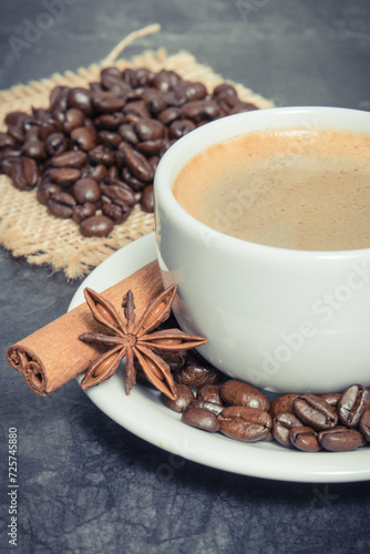 Coffee in white cup and roasted dark coffee beans with seasonings