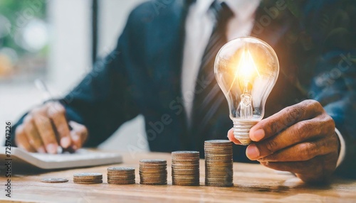 creative ideas for saving money concept businessman holding lightbulb with stack of coins on the table planning to manage future financial growth