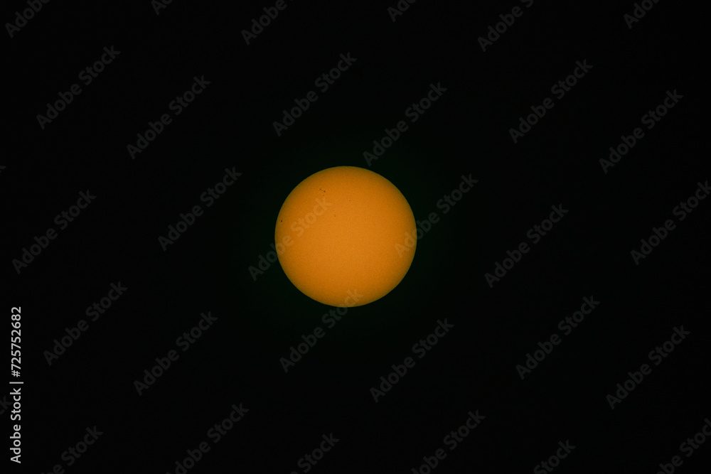 Tarcza słoneczna sfotografowana z użyciem teleobiektywu. W wyniku zastosowania filtra optycznego uzyskano ciepłą barwę tarczy słonecznej. Widoczne są plamy na powierzchni słońca. - obrazy, fototapety, plakaty 